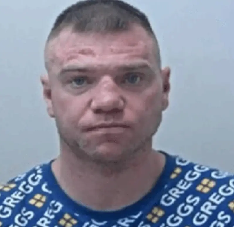A wanted man who was photographed in his mugshot wearing a Greggs jumper has been apprehended