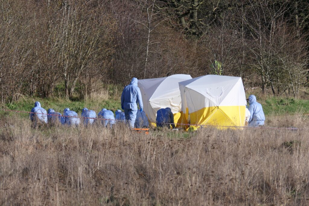 Forensic team investigating site with tent in field.