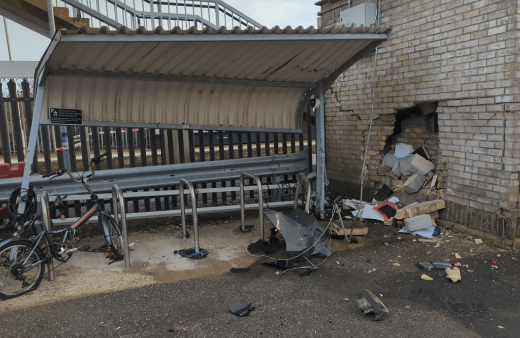 Damaged bicycle parking area with debris and broken wall.