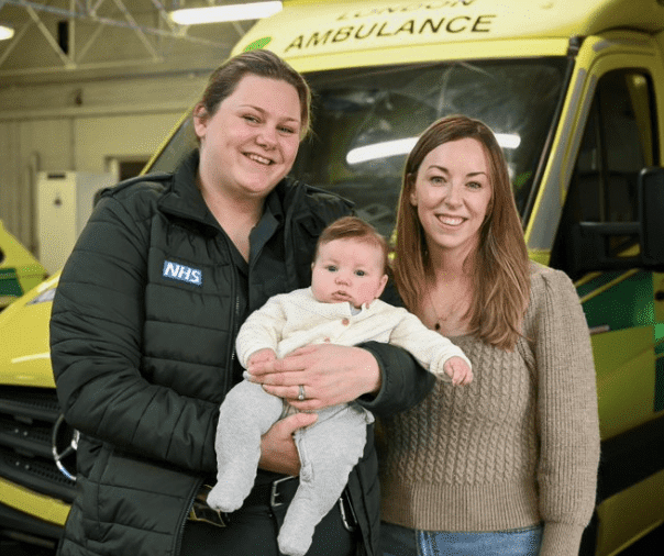 Two women and baby in front of NHS ambulance.