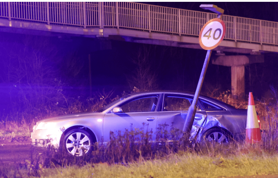 Damaged car near 40mph sign under bridge at night.