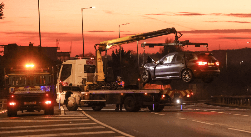 Flatbed truck towing car at sunset on highway.