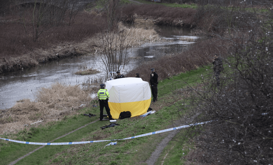 Police investigation near river with crime scene tent.