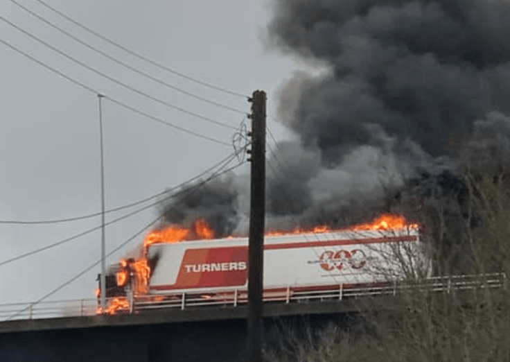 Lorry ablaze on bridge with heavy smoke.