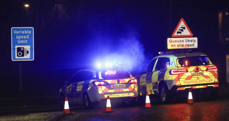 Police cars blocking road at night with emergency lights on.