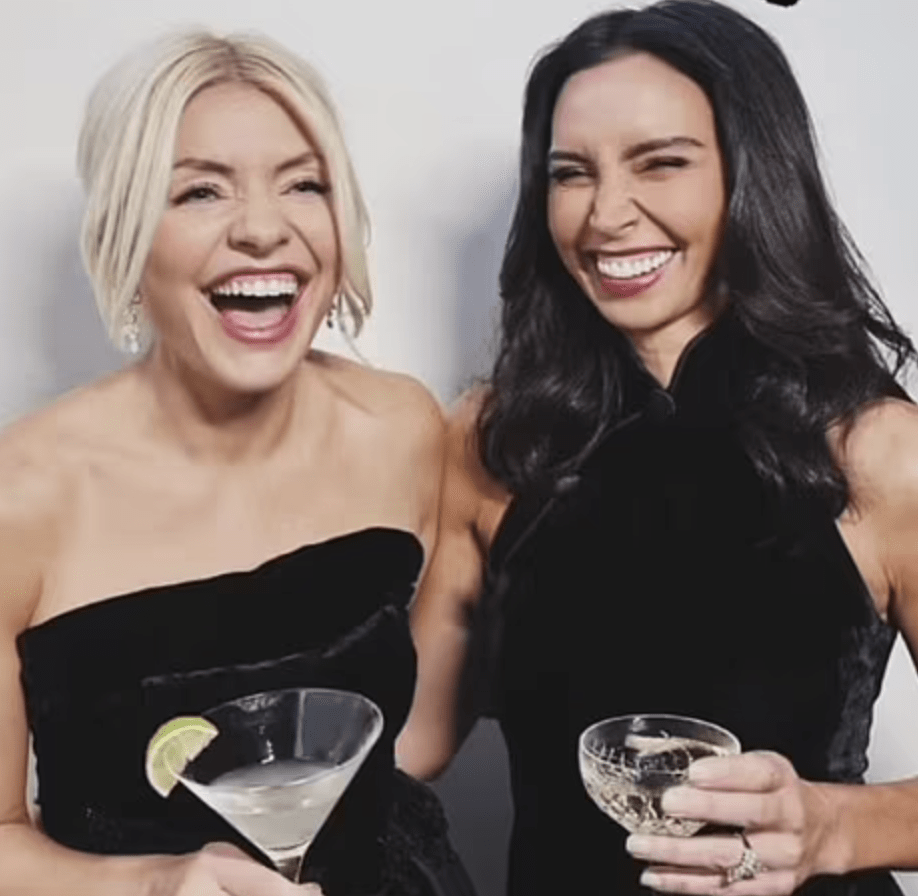 Two women laughing and holding drinks at elegant event.
