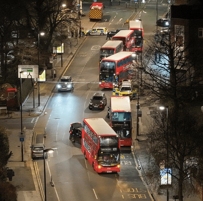 Night-time street view with red buses and emergency vehicle.